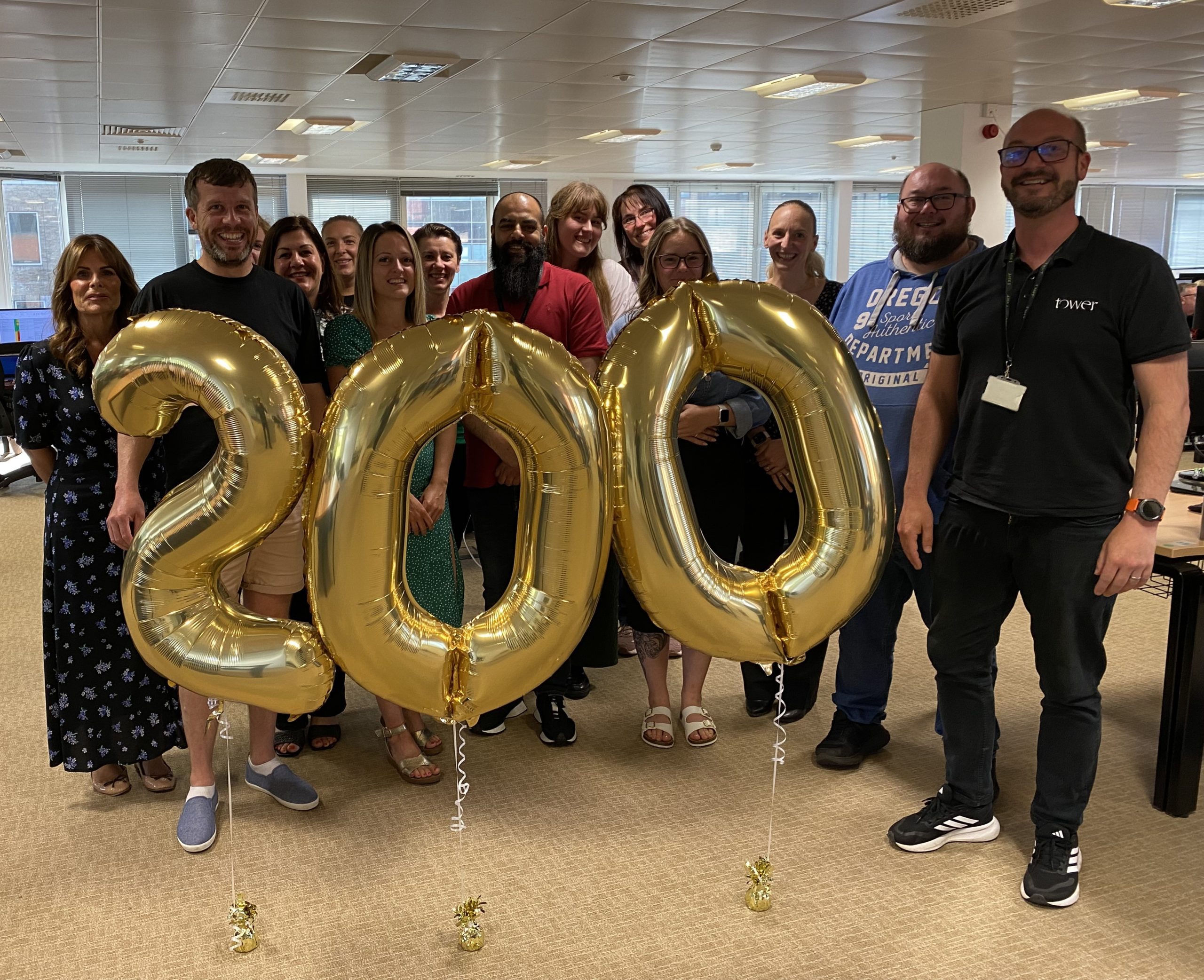 A photo of the Tower Leasing team behind three gold balloons displaying 200