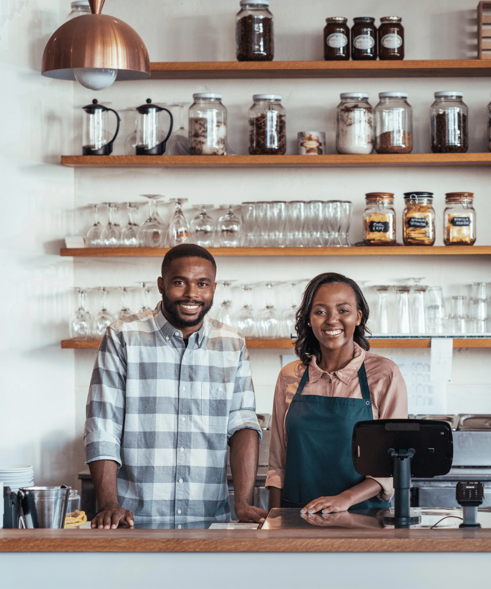 Two business owners stand smiling behind their counter