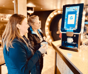 Two customers wait at a Lua Bean to Cup machine as it fills up their coffee cup.
